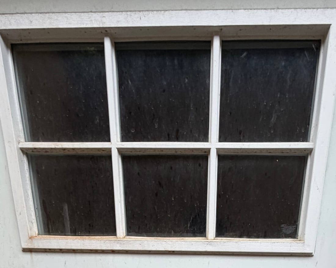 A door window before cleaning — the glass is hazed over with dust and dried water spots you can barely see through.